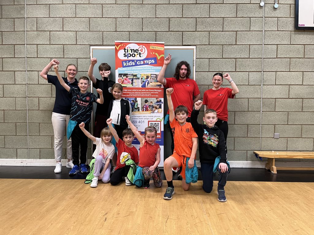 A group of Time4Sport leaders and children face the camera, raising their fists and smiling.