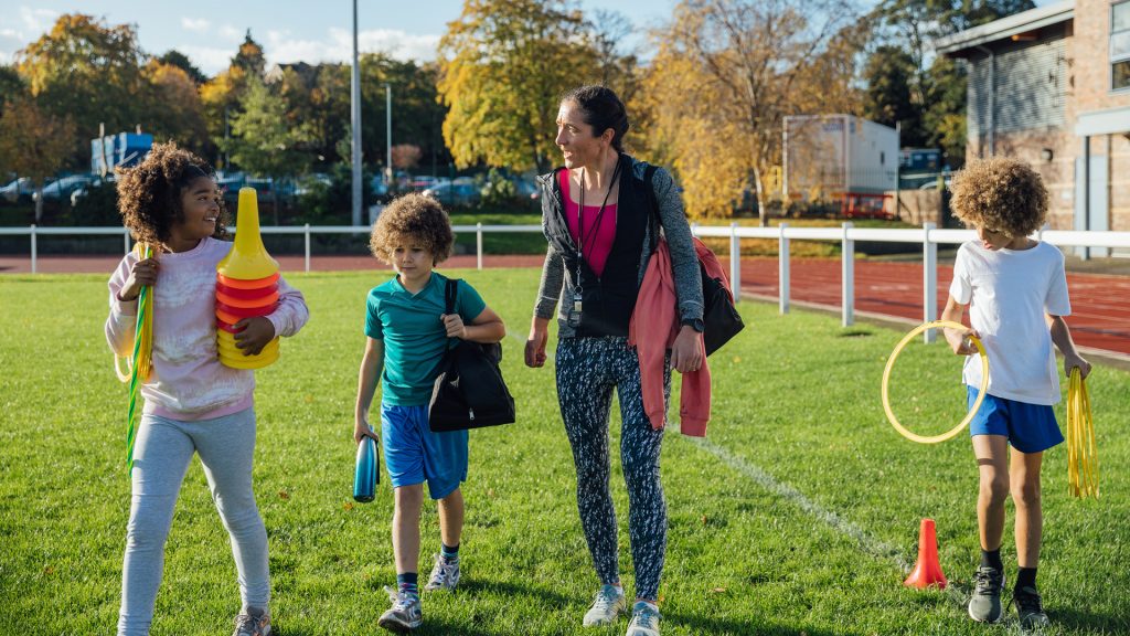 Female coach and a group of children on grass sports field.